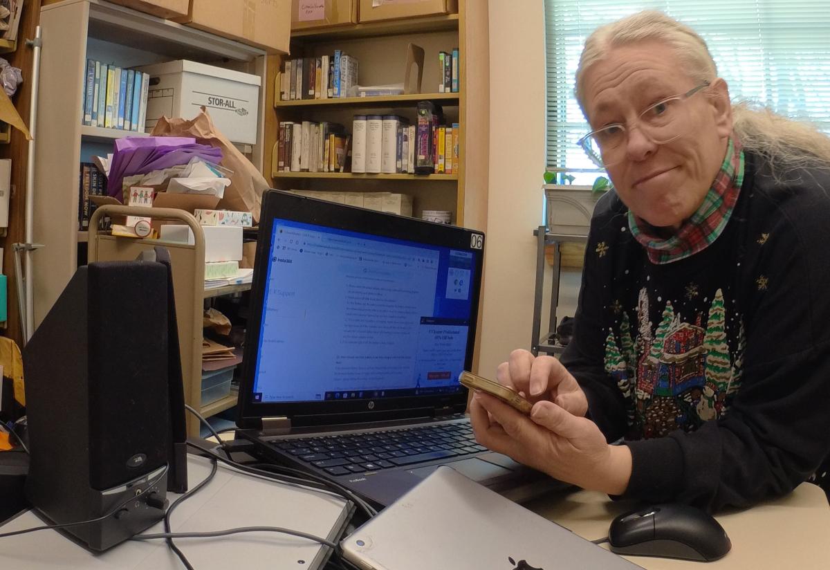 Julia holding a phone with tablets and laptops on a table